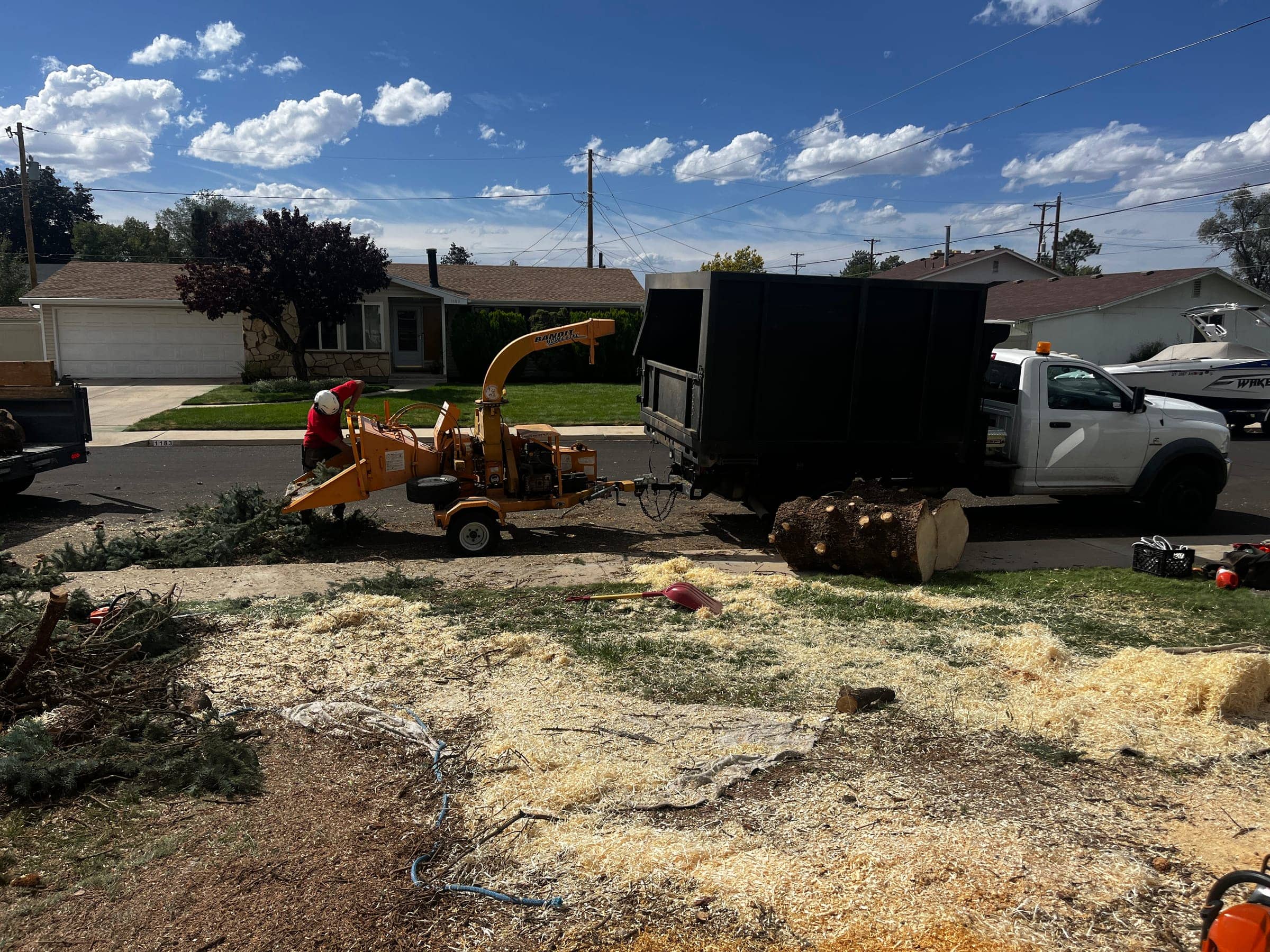 Crew member feeding branches into a chipper beside a dump truck on a residential street